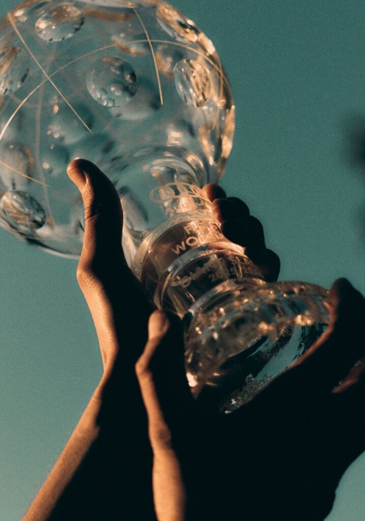 Hands holding a crystal trophy against a clear blue sky.