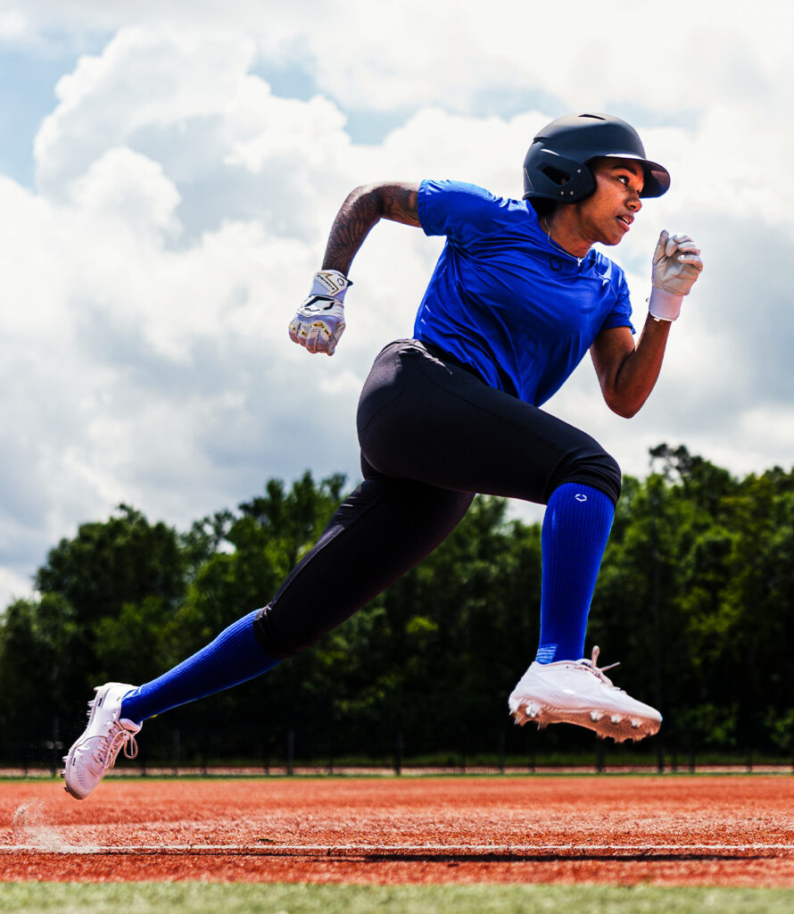 Athlete wearing blue EvoShield baseball or softball apparel sprinting across an outdoor field.