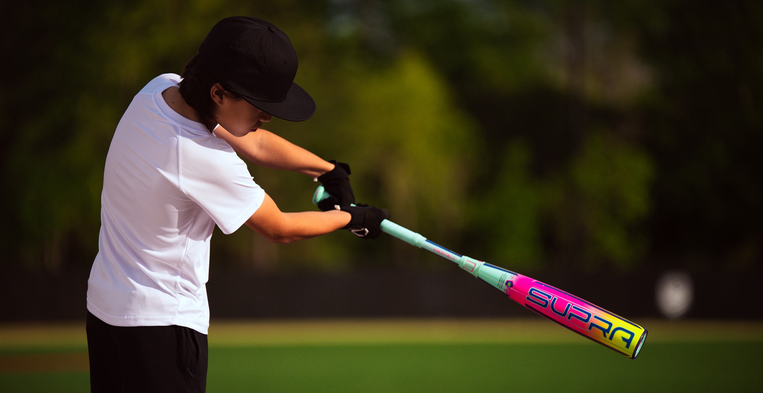 Young man swinging a Louisville Slugger bat on a green field