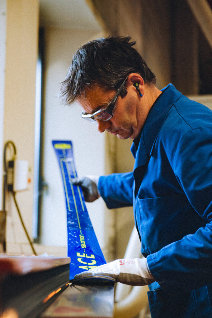 A factory worker skillfully works on Salomon's blue alpine ski.