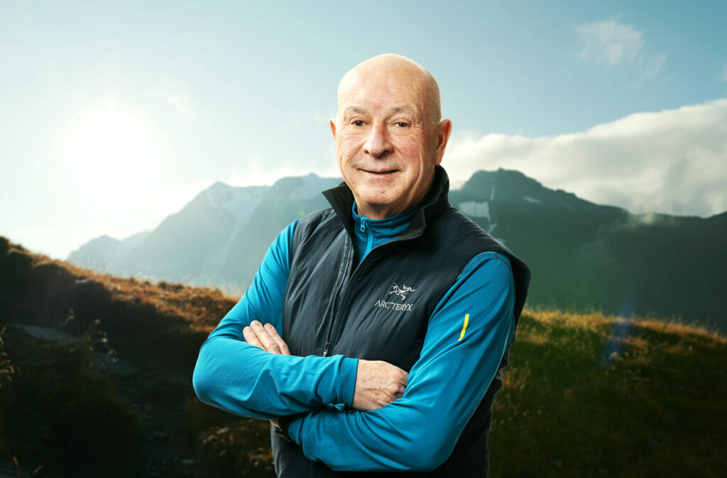 Portrait of Michael-Schineis standing in front of a mountain wearing a blue shirt and black Arc'teryx vest.