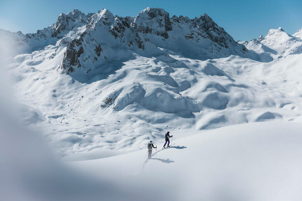 Two skiers photographed in the distance in front of a big snowy mountain