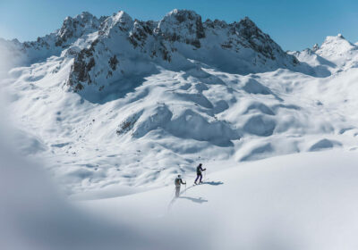 Two skiers photographed in the distance in front of a big snowy mountain