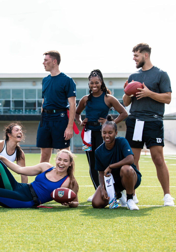 Six young American football players are smiling on the grass.