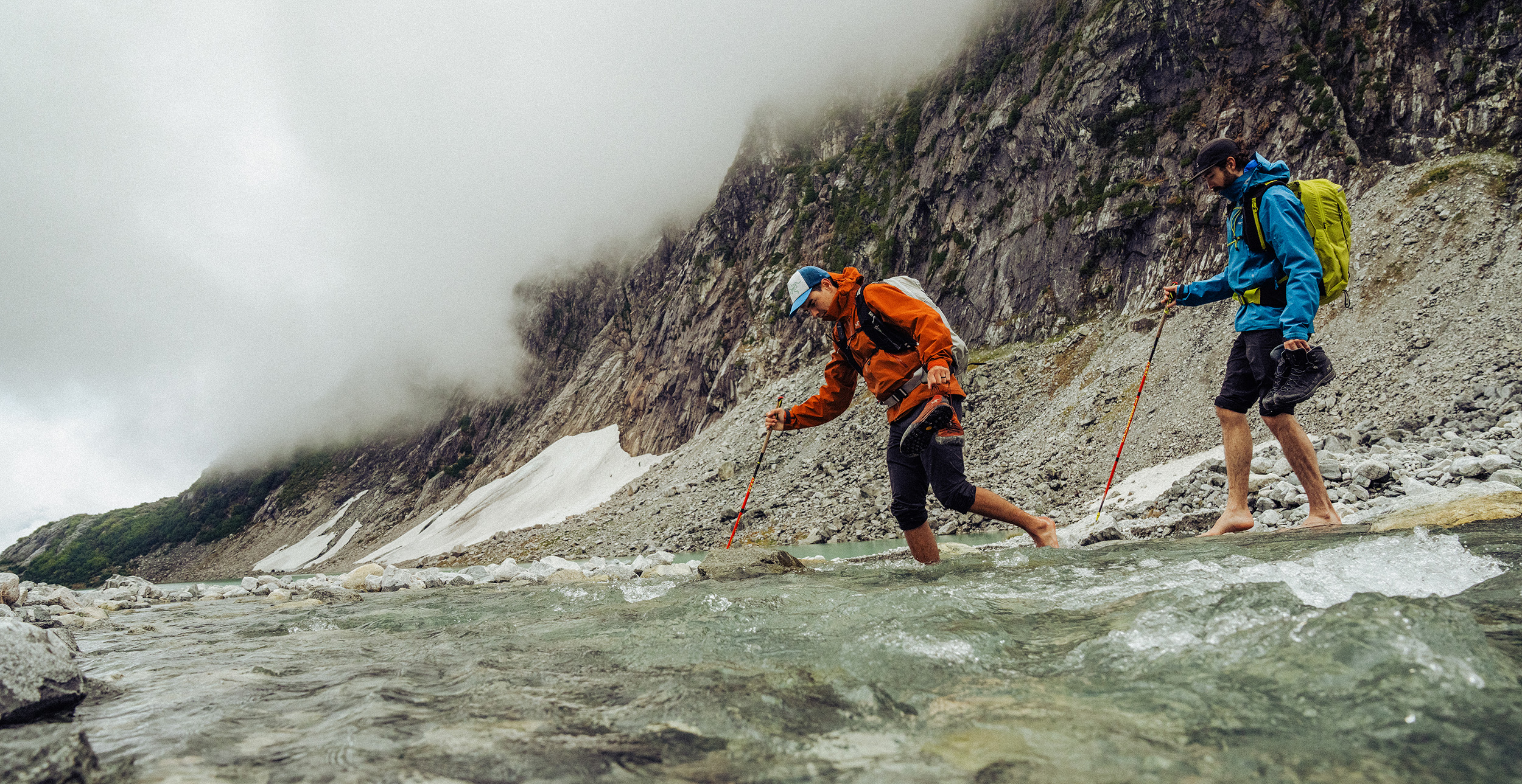 Two people crossing a river in a mountain valley by foot.