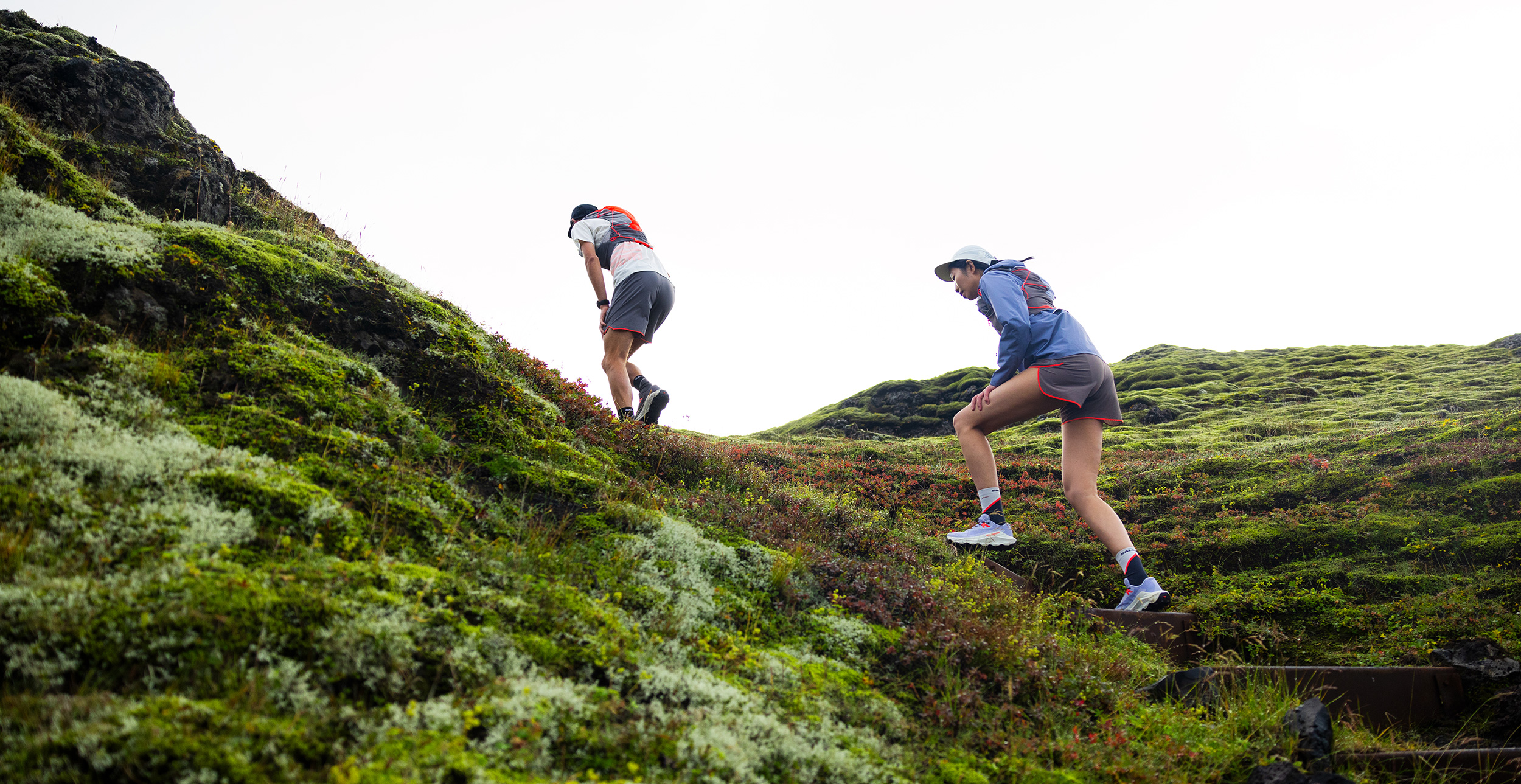Two people hiking on green hills.