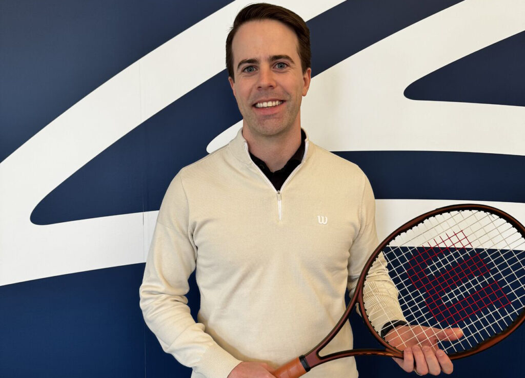 Man smiling, holding a tennis racket