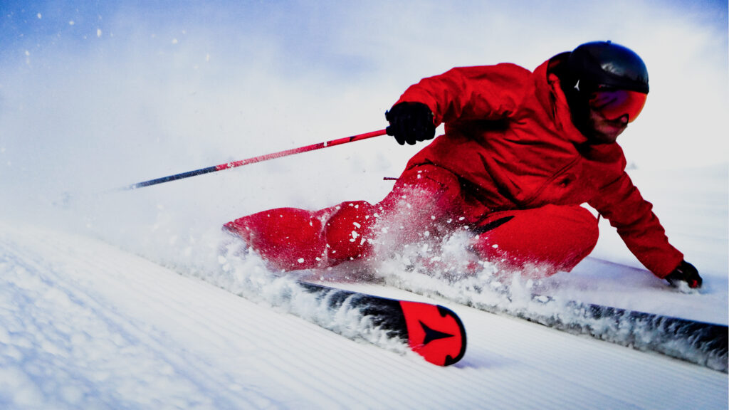 Person in bright red ski gear carving through snow on a slope.