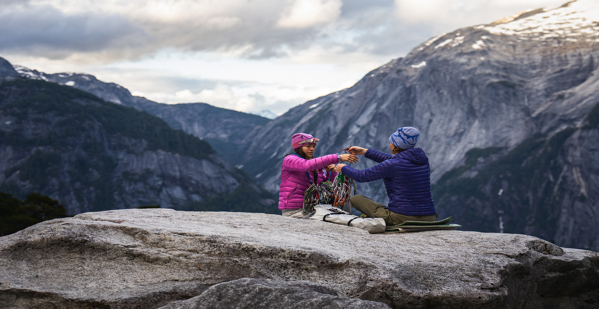 Two women sitting on top of a mountain handling climbing ropes.