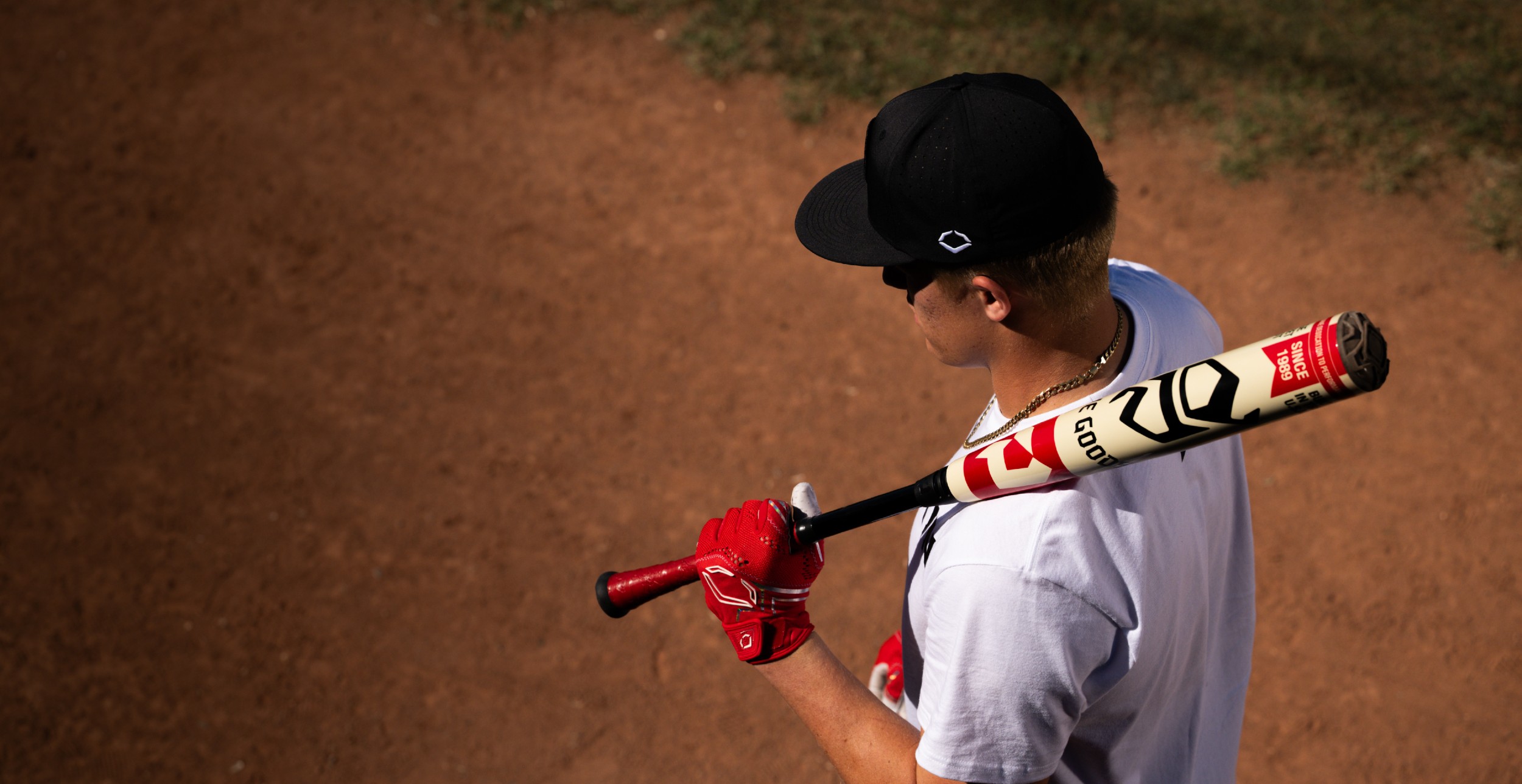 Baseball player carrying a DeMarini bat over one shoulder on a dirt field.